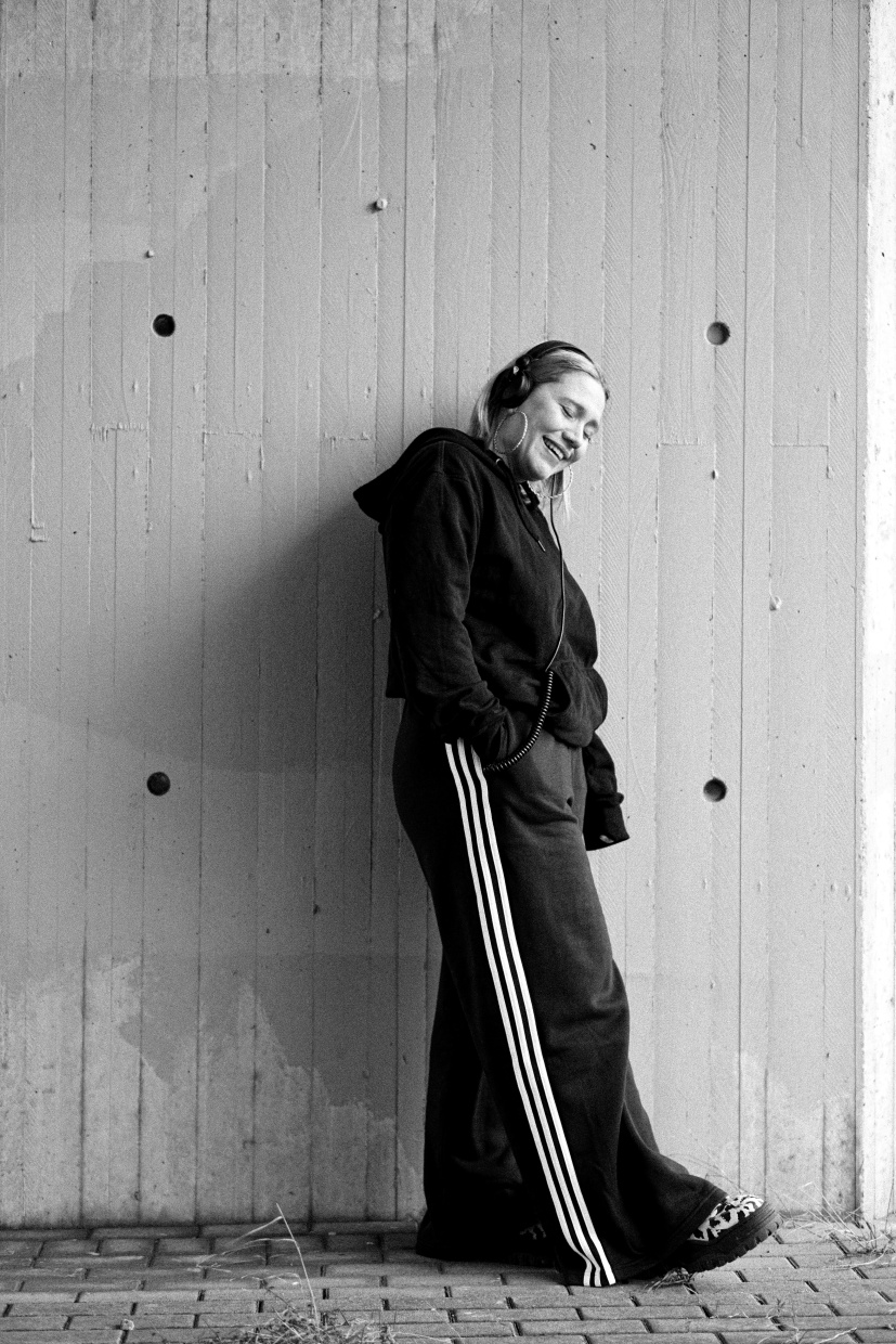 Mann in schwarzer Jacke lehnt an grauer Betonwand, Schwarzweißfotografie.