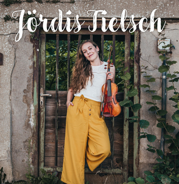 Musikerin steht mit Geige i der Hand draußen vor einer Wand