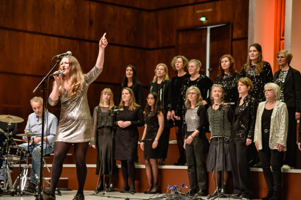 eine Frau im silbernen Kleid leitet einen Chor an