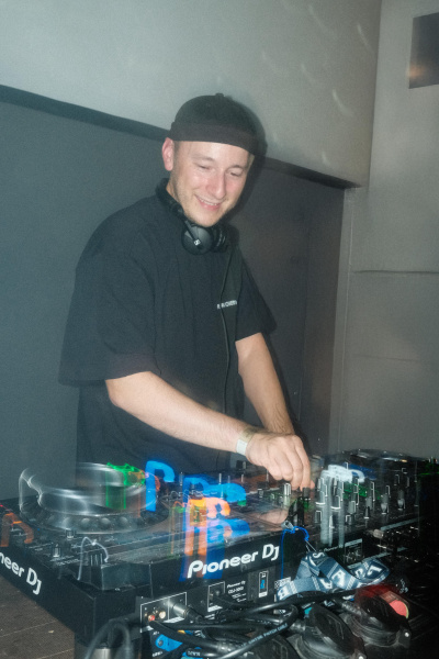 DJ an Mischpult mit Kopfhörern und schwarzem Shirt.