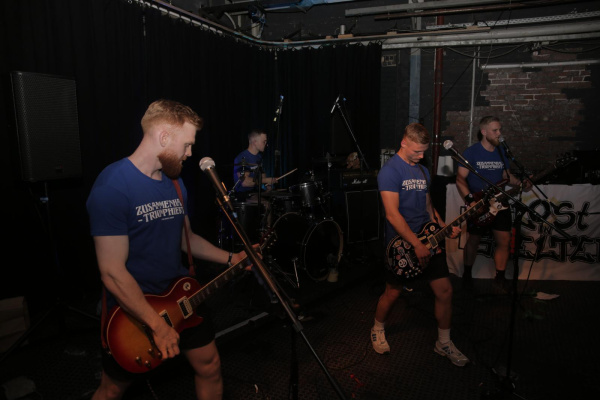 Rockband spielt live auf dunkler Bühne mit Gitarristen und Publikum.