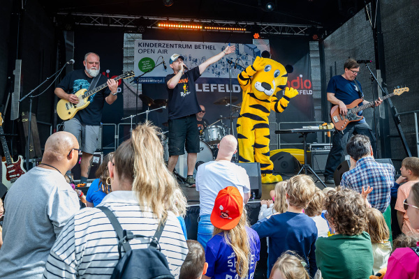 Musikband spielt auf Bühne vor Publikum mit Kindern im Vordergrund.