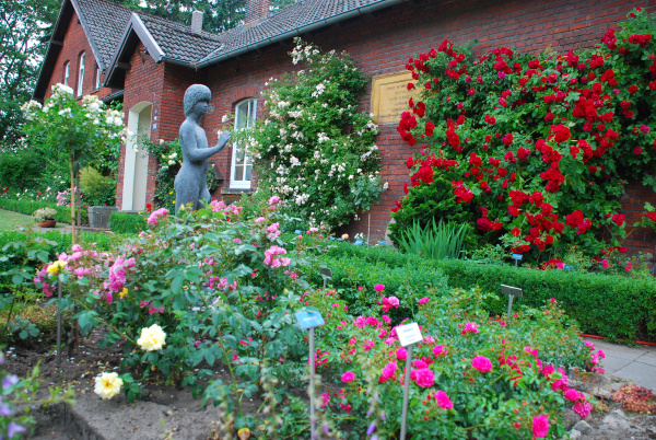 Buntes Rosenbeet mit Frauenskulptur vor der Museumsschule