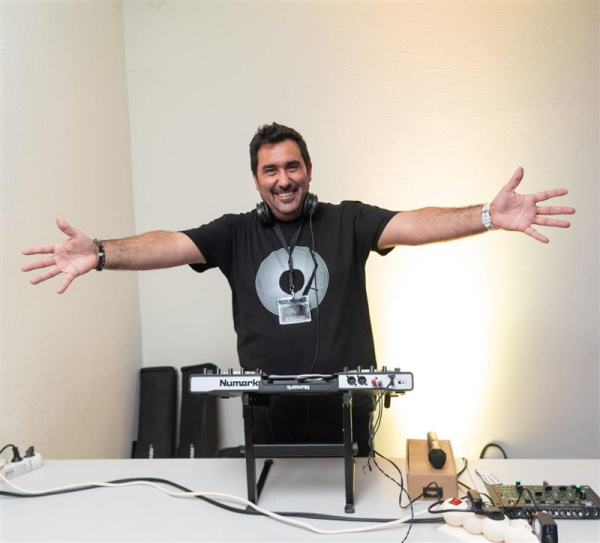 DJ mit ausgebreiteten Armen an Mischpult, Studio-Setup mit Equipment.