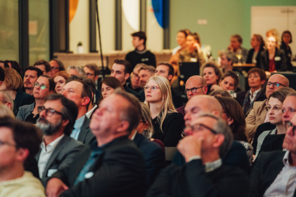 Publikum in der Wissenswerkstadt, welches Aufmerksam etwas ansieht, was auf dem Bild nicht zu sehen ist.