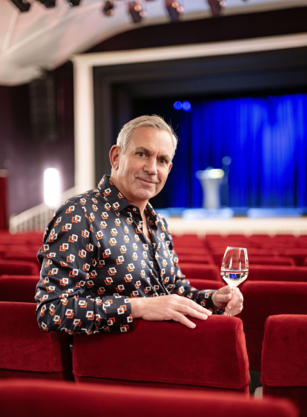 Wladimir Kaminer sitzt mit einem Glas in der Hand auf einem Kinosessel
