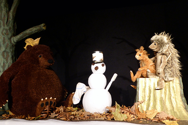 Eichhorn, Bär und Igel sitzen vor einem Schneemann