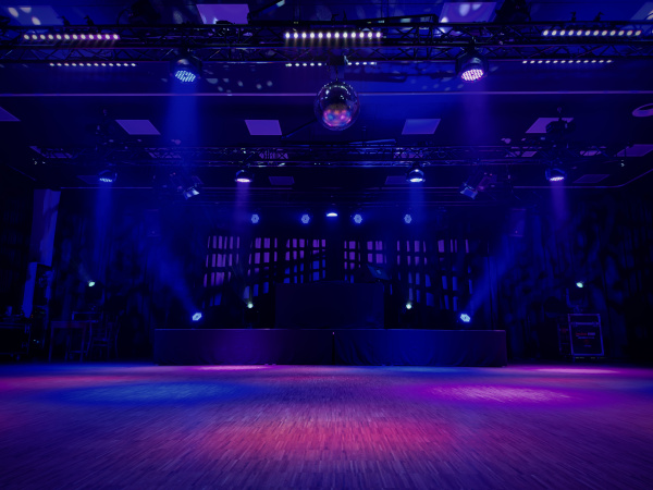 Das bild zeit eine bunt beleuchtete Tanzfläche und Bühne. In der Mitte hängt an der Decke eine Disko