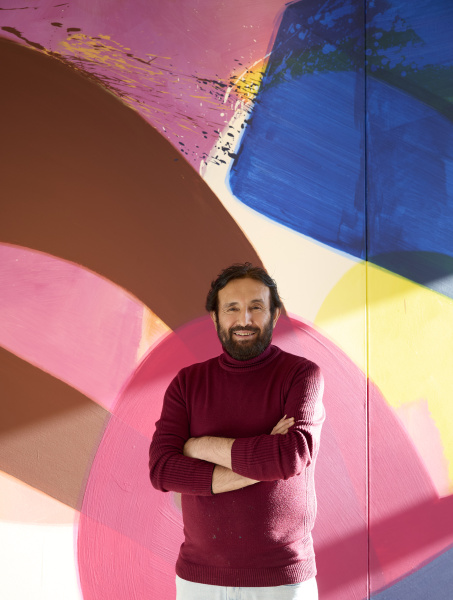 Der Künstler Aatifi vor einer großen, farbenfrohen Malerei. 