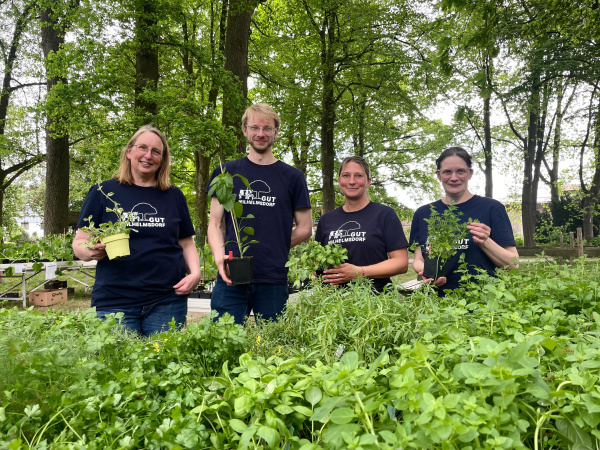 Das Wilhelmsdorfer-Pflanzmarkt-Team präsentiert verschiedene Jungpflanzen vor vollem Pflanztisch.