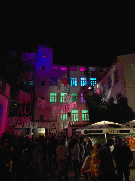 Impression der Benefizparty bei Nacht mit beleuchteten Fenstern und Menschen im Innenhof des Vereins