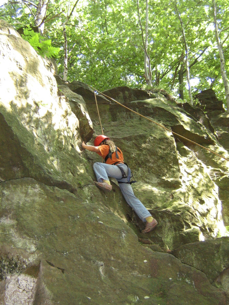 Kind mit Klettergurt am Seil gesichert klettert den Felsen hoch