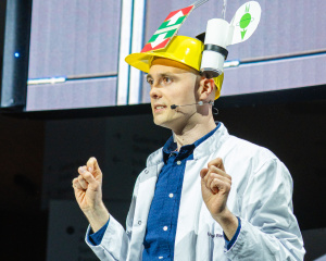Mann mit gelbem Helm gestikuliert vor Publikum.
